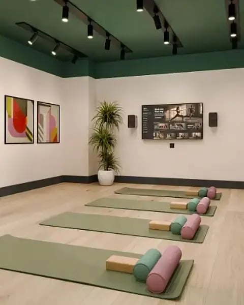 On-site wellness studio with green yoga mats, blocks and bolsters laid out on a wooden floor, a wall-mounted fitness screen and colourful artwork.