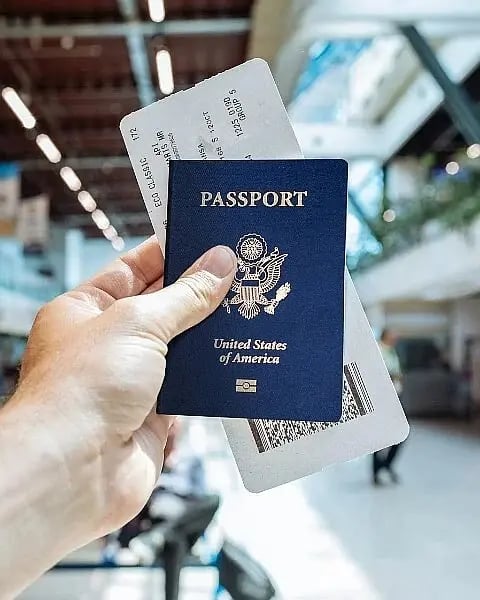 Hand holding a passport and boarding pass in a bright airport terminal.